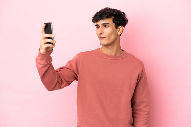 Fiatal argentin férfi elszigetelt rózsaszín háttér csinál egy szelfi - Fotó, kép