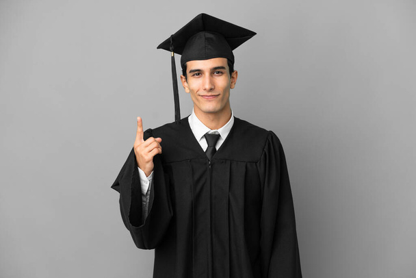 Mladý argentinský univerzitní absolvent izolovaný na šedém pozadí ukazující ukazováčkem skvělý nápad - Fotografie, Obrázek