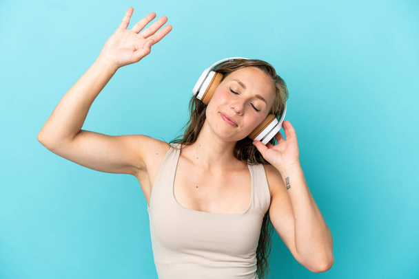 Young caucasian woman isolated on blue background listening music and dancing - Foto, afbeelding
