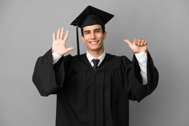 若いアルゼンチンの大学の卒業生は指で6を数える灰色の背景に隔離されました - 写真・画像