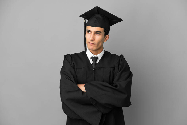 若いアルゼンチンの大学の卒業生は、肩を持ち上げながら疑問ジェスチャーを作る灰色の背景に隔離されました - 写真・画像