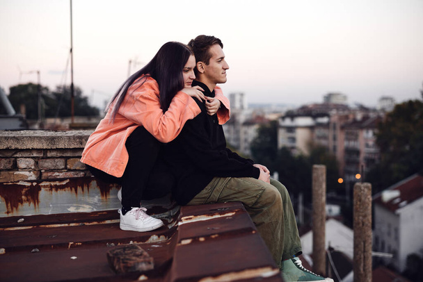 Nastoletnia para siedzi na dachu budynku, patrząc na widok i przytulając. - Zdjęcie, obraz