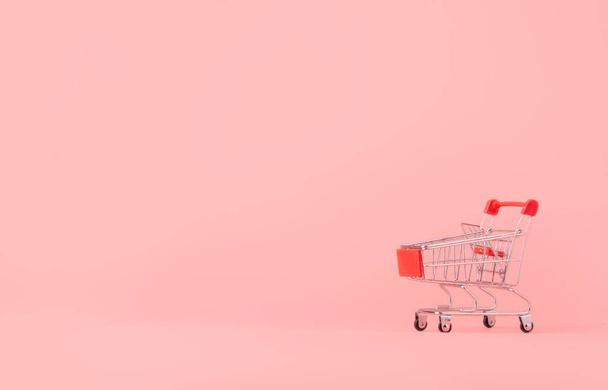 Vásárlási koncepció: Üres piros bevásárlókocsi rózsaszín háttérrel. online vásárlás fogyasztók vásárolhatnak otthonról és a szállítási szolgáltatás. fénymásolási hellyel - Fotó, kép