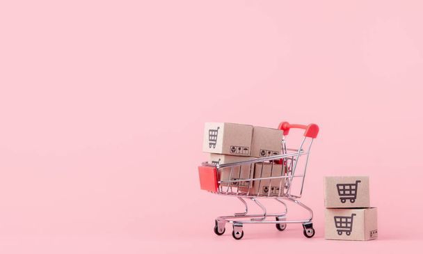 Ostoskonsepti: Pahvilaatikot punaisessa ostoskärryssä vaaleanpunaisella taustalla. verkkokaupoissa kuluttajat voivat tehdä ostoksia kotoa ja jakelupalvelusta. kopiotilaa - Valokuva, kuva