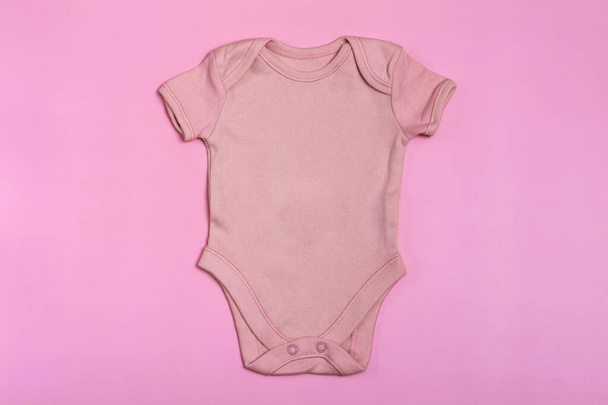 ピンクの空白のベビーボディスーツテンプレート、ピンクの背景にクローズアップモックアップ。赤ちゃんの体のスーツ新生児のためのジャンプスーツ。上からの眺め - 写真・画像