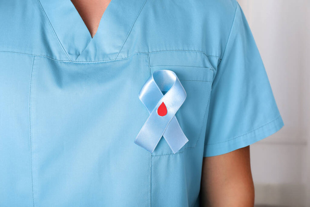 Doctor with light blue ribbon and paper blood drop indoors, closeup. World Diabetes Day - Zdjęcie, obraz