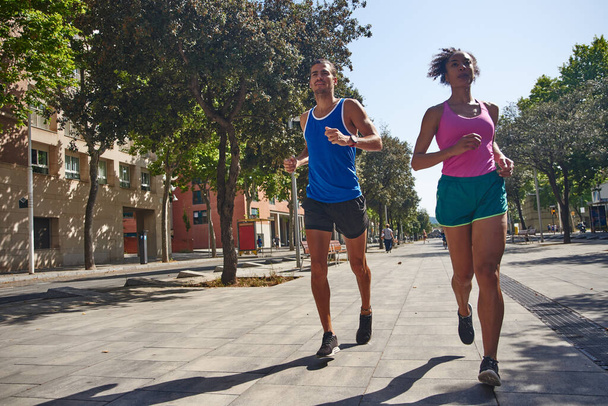 Sporty ethnic couple running together during the morning training session outdoors in the city - Фото, изображение