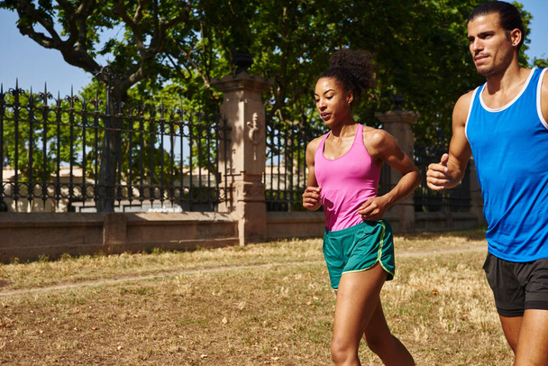 Dedicated young couple running together in gym clothing outdoors during the day - Фото, изображение