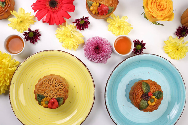 Colorful flower decorated moon cake Chinese mid autumn festival tea in small white teacup chopsticks plates bowl blue yellow violet chrysanthemum mum red daisy flower on white background - Photo, Image