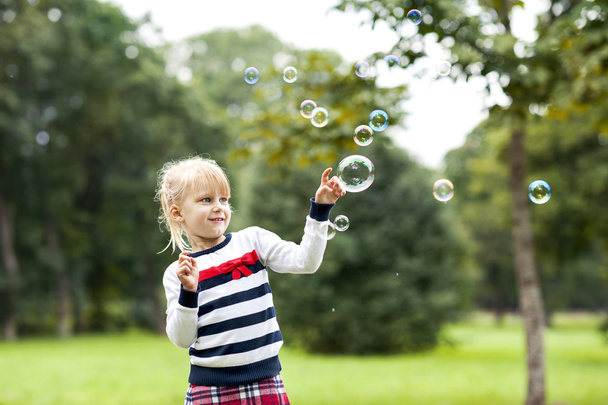 kleine blonde spelen meisje met zeepbellen in groene zomer par - Foto, afbeelding