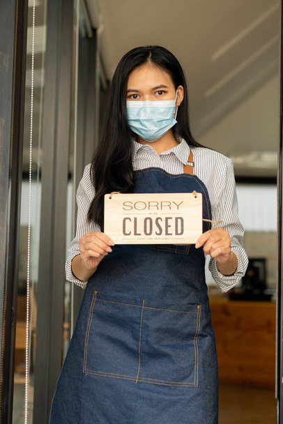 Frau blättert Ladenschild um Ein geschlossenes Schild hängt an der Glastür. Geschlossene Banner werden von schönen asiatischen Frauen nach der Arbeit oder während des COVID-19-Ausbruchs in der Stadt getragen. - Foto, Bild