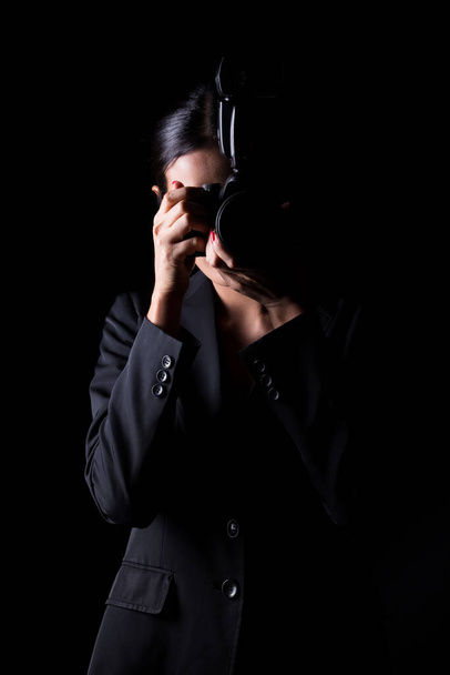 Ázsiai nő fotós tartsa kamera külső flash pont lőni téma, viseljen formális öltöny. stúdió világítás fekete háttér elszigetelt másolás tér, riporter újságíró fotózás híresség - Fotó, kép