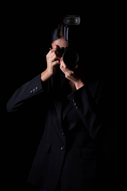アジアの女性写真家は被写体を撮影する外部フラッシュポイントとカメラを保持し、正式なスーツを着用します。スタジオ照明黒背景隔離されたコピースペース記者ジャーナリスト写真有名人を取る - 写真・画像