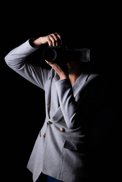 Asian Woman Photographer hold camera with external flash point to shoot subject, wear gray suit. studio lighting black background isolated low key exposure, reporter journalist take photo celebrity - 写真・画像
