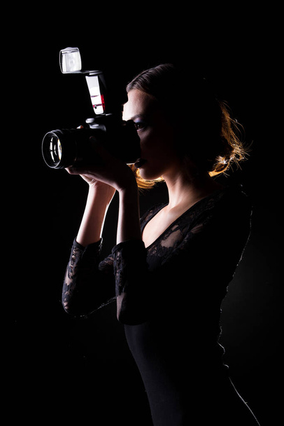 Asian Woman Photographer hold camera with external flash point to shoot subject, wear body suit. studio lighting black background isolated low key exposure, reporter journalist take photo celebrity - Photo, Image