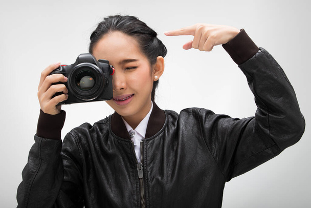 Φωτογράφος κρατήσει φωτογραφική μηχανή με το σημείο φακό για να πυροβολήσει το θέμα, φορούν κανονική σκούρο μαύρο σακάκι leater κοστούμι. Φωτισμός στούντιο λευκό κλίση γκρι φόντο απομονώνονται, τα δάχτυλα σημείο λένε Hey ματιά σε αυτή την κάμερα - Φωτογραφία, εικόνα