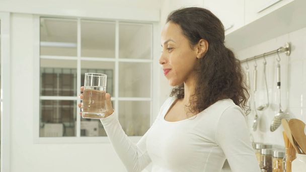 Portret van een gelukkige vrouw die thuis een glas water drinkt in de keuken. Mensen hun levensstijl. Versheid. - Foto, afbeelding