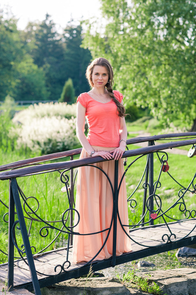 όμορφη γυναίκα να στέκεται σε ένα πάρκο κοντά στη γέφυρα - Φωτογραφία, εικόνα