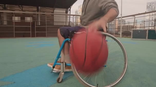 Niski kąt łuk przyciętego sportowca na wózku inwalidzkim dryblingu na boisku do koszykówki w okolicy - Materiał filmowy, wideo