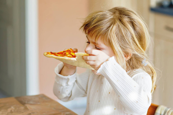 Roztomilé batole dívka jíst italskou pizzu se zeleninou a sýry. Happy dítě jíst čerstvé vařené zdravé jídlo s rajčaty, kukuřicí a zeleninou doma, uvnitř. - Fotografie, Obrázek