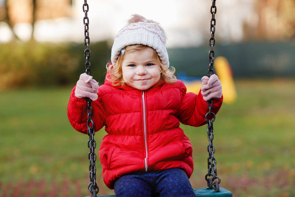 Cute toddler girl having fun on playground. Happy healthy little child climbing, swinging and sliding on different equipment. On cold day in colorful clothes. Active outdoors game for children - Photo, Image