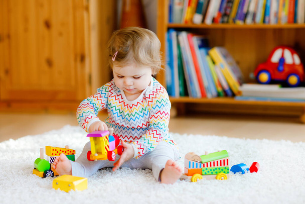 little baby girl playing with educational wooden toys at home or nursery. Toddler with colorful train. Child having fun with different toys. Lonely kid during corona virus pandemic quarantine - Фото, изображение