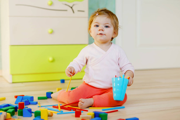 教育用のおもちゃで遊ぶかわいい赤ちゃんの女の子。自宅や保育園でカラフルな異なる木製のブロックで楽しんでいる幸せな健康的な子供。赤ちゃんのクロールと色や形を学びます,屋内 - 写真・画像