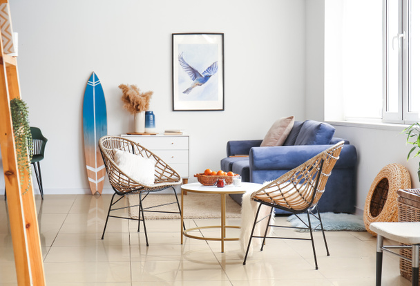 Belső tér modern elegáns szoba asztallal, fonott fotelek, kanapé és szörfdeszka - Fotó, kép