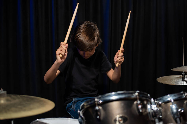 The boy learns to play the drums in the studio on a black background. Music school student - Foto, Imagen