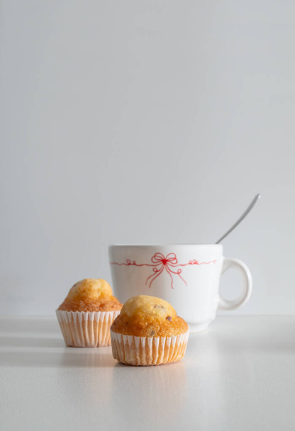 A vertical shot of two small chocolate chip muffins, and a mug on a white background with copy space - Φωτογραφία, εικόνα
