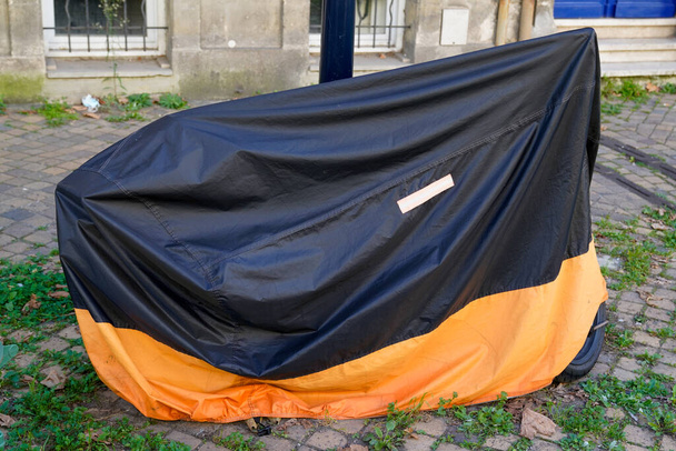 moto protegida por naranja y negro cubierta de plástico protector bicicleta en la ciudad motocicleta de calle con chaqueta de lona - Foto, Imagen