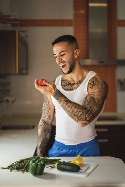 A vertical shot of a tattooed Caucasian male athlete preparing healthy food in the kitchen - Foto, afbeelding