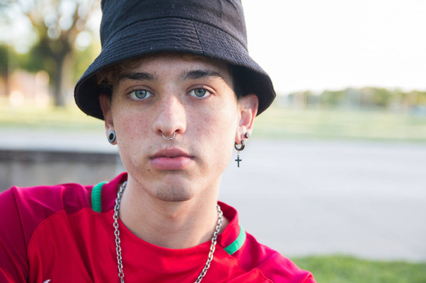 A portrait of a cool young Argentine man with earrings and a piercing wearing a bucket hat outdoors - Фото, зображення
