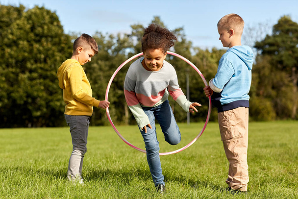 happy children playing game with hula hoop at park - Foto, Bild