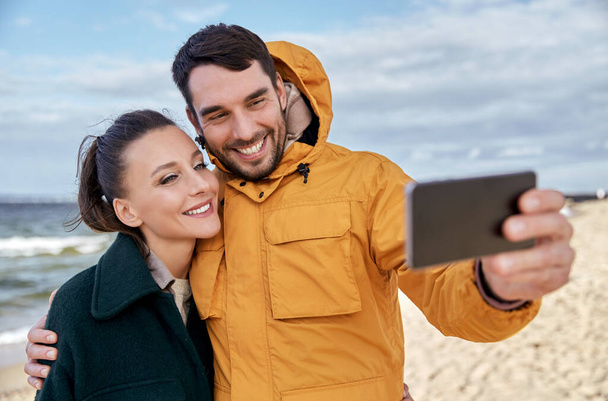 couple with smartphone on autumn beach - Photo, Image