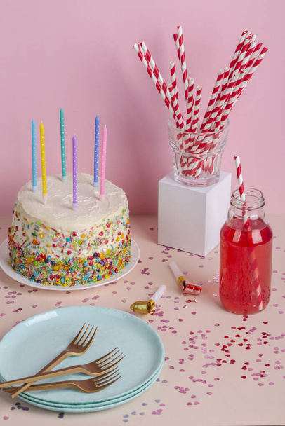 Pionowe ujęcie tortu ze świecami, talerzami, widelcami, słomkami i napojem na dziecięcej imprezie - Zdjęcie, obraz