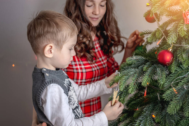 Mom with her child is decorating together the Christmas tree with toys and balls. Concept of family preparation for the New Year, cozy atmosphere and festive mood. - Φωτογραφία, εικόνα