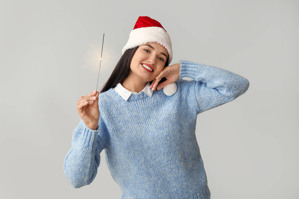 Young woman with Christmas sparkler on grey background - Photo, Image