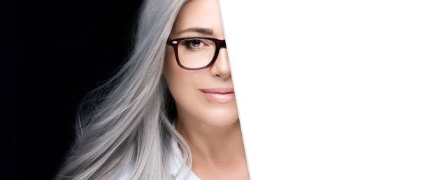 Mujer de pelo gris con gafas en un retrato de media cara con cartón blanco al lado. Agudeza, pruebas visuales, oftalmología, miopía, hipermetropía o astigmatismo - Foto, Imagen