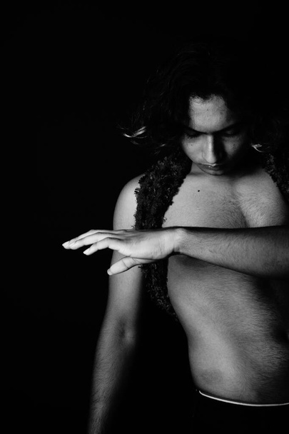 A Greyscale shot of a half-naked South Asian male with a feather scarf and wig - Фото, зображення
