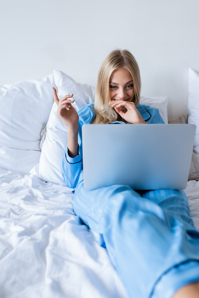 joyful young woman in pajamas watching comedy movie on laptop in bedroom - Foto, imagen