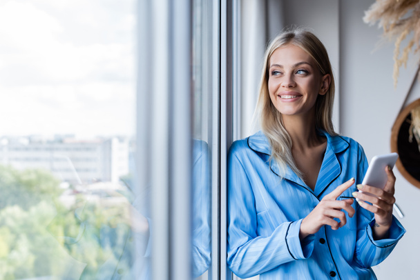 happy young woman holding cellphone and looking at window  - Photo, Image