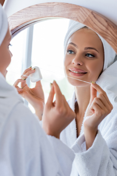 young and cheerful woman in bathrobe holding dental floss near mirror  - Photo, Image