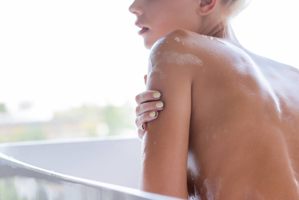 vue recadrée de jeune femme humide avec de la mousse sur le corps prenant un bain  - Photo, image