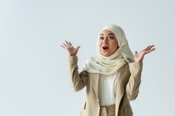 amazed muslim woman in hijab and beige suit gesturing isolated on grey - Foto, immagini