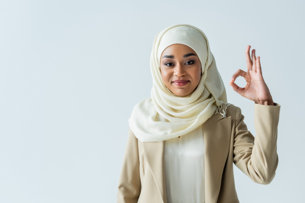 happy muslim woman in hijab showing ok sign and smiling isolated on grey - Foto, Imagem