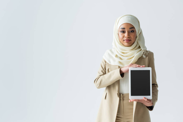  ヒジャーブ州のイスラム教徒の女性はグレーで隔離された空白の画面を持つデジタルタブレットを保持 - 写真・画像