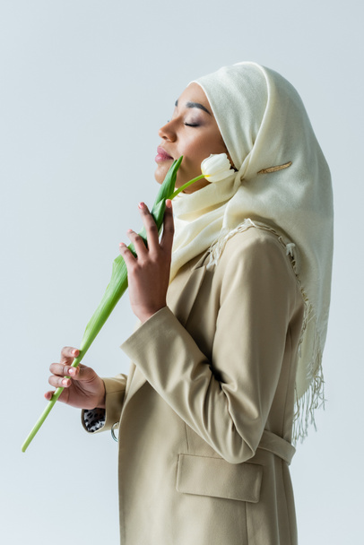 muslim woman with closed eyes holding tulip isolated on grey - Fotó, kép