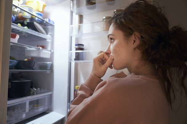 Döntetlen fiatal kaukázusi nő ellenőrzi a hűtőszekrényt, hogy van-e ennivaló éjszaka. - Fotó, kép