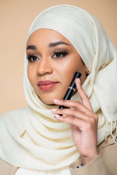 hübsche muslimische Frau im Hijab hält Mascara isoliert auf beige - Foto, Bild